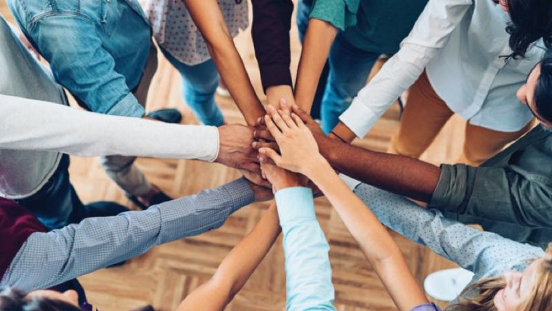 Twelve people placing their hands together in the center of a circle