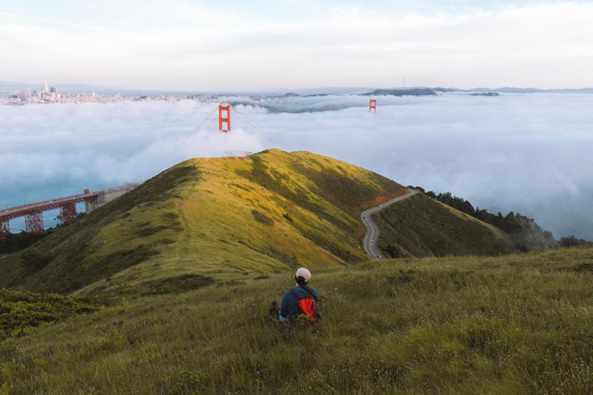 Person sitting the grass looking the Golden Gate Bridge obscured by fog