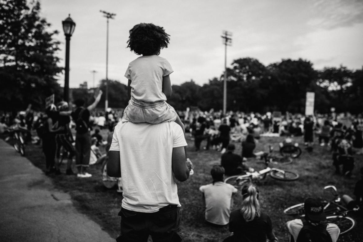 Person with a child on their shoulders looking at a protest or gathering