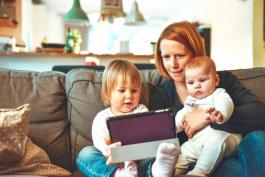 Woman sitting with two small children on a couch while looking at a tablet device