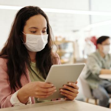 Masked person looking at tablet while seated